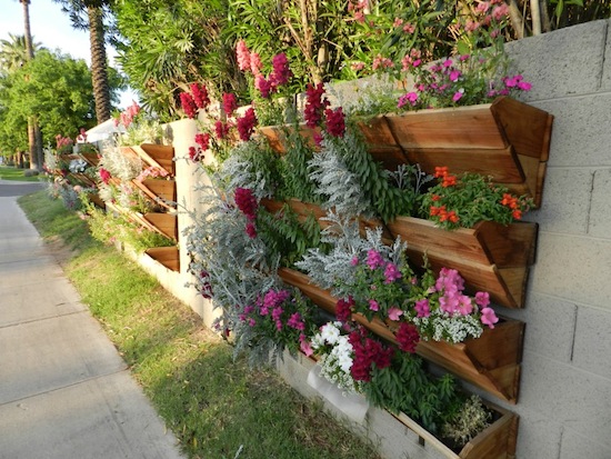 A vertical garden with flowers is displayed outdoors alongside a sidewalk.