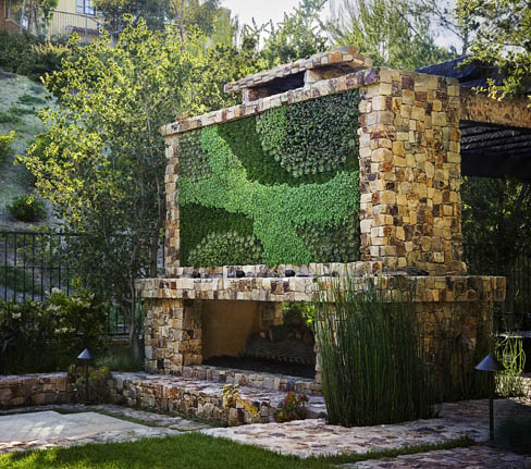 A stone fireplace in an outdoor backyard with a green wall and a vertical garden.