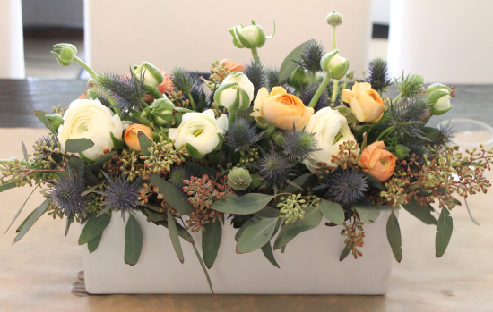 A winter floral arrangement in a white box on a table.