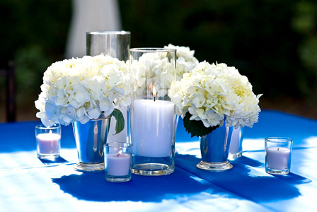 A table adorned with white winter floral arrangements and candles on a blue tablecloth.