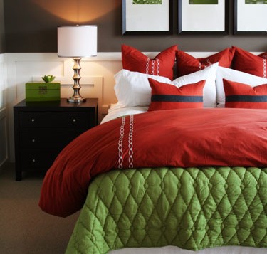 A guest bedroom with a red and green comforter.