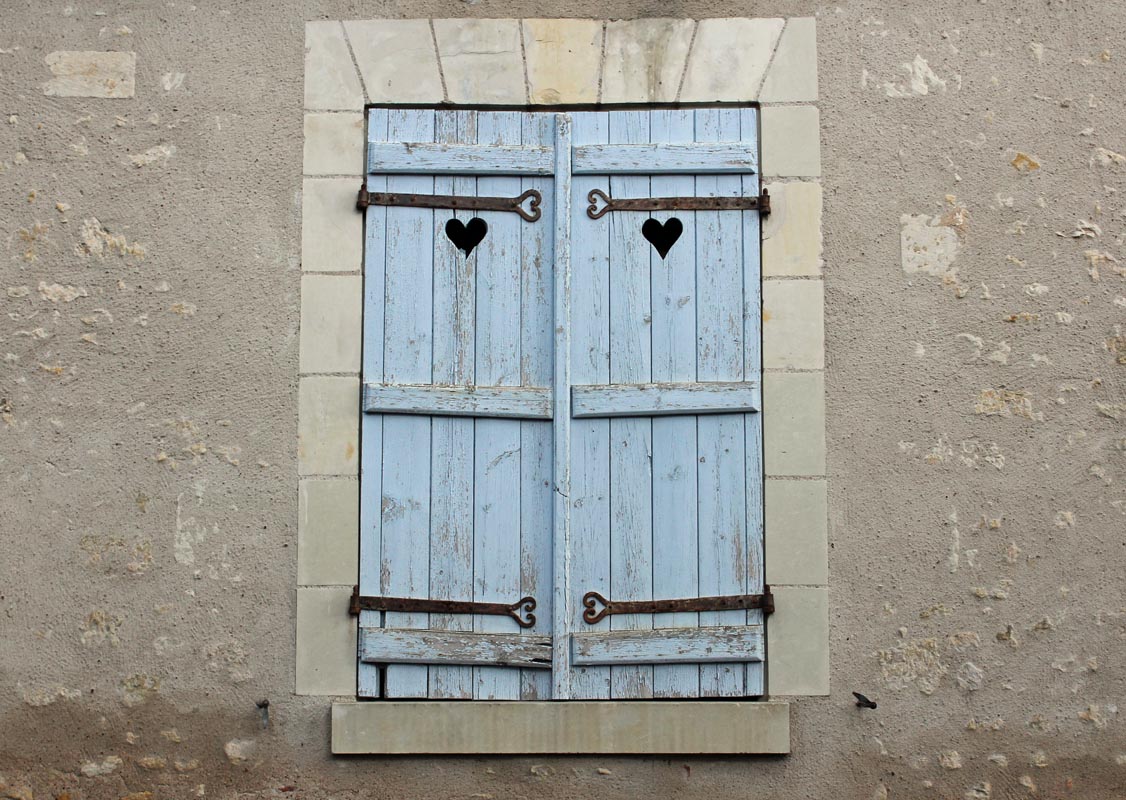 Two beautiful blue shutters with hearts on them on a stone wall.