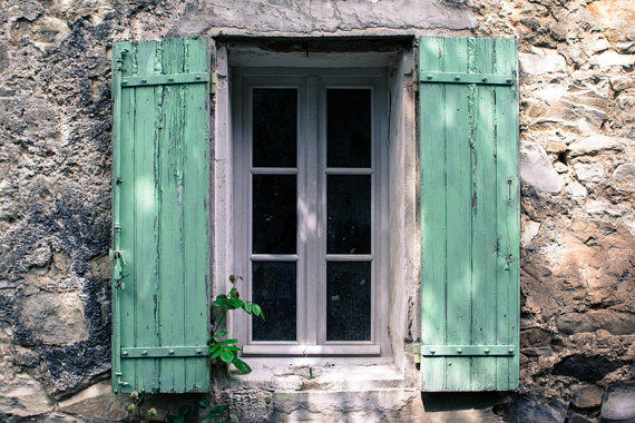 A beautiful window with green shutters on a stone wall.