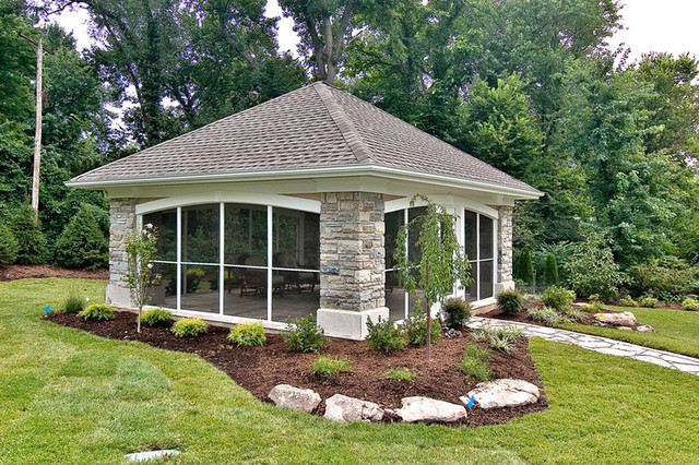 A stone gazebo in the middle of a yard.