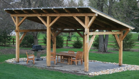 A wooden backyard pavilion with a bbq and picnic table.
