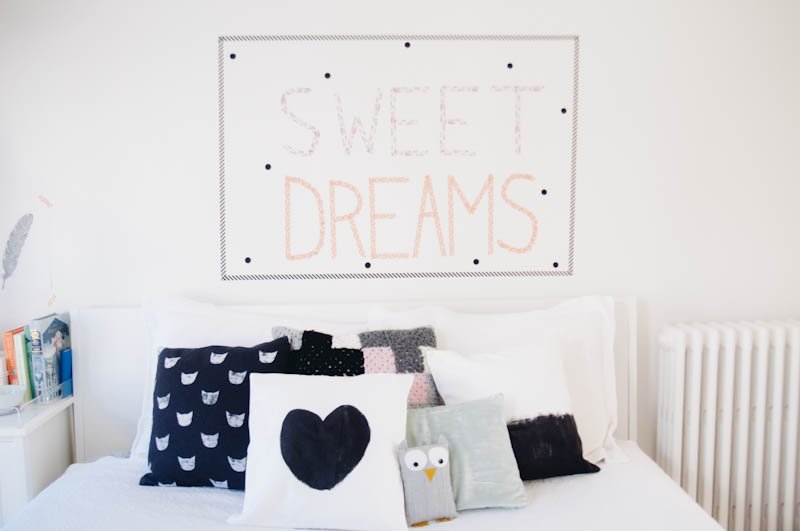 A white bed with pillows and a DIY pillow sign that says sweet dreams.