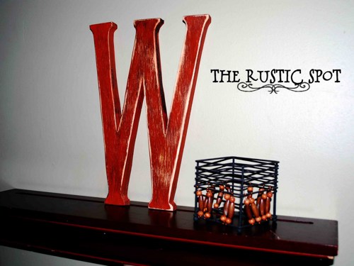 A decorative wooden letter w sits on a shelf next to a candle.