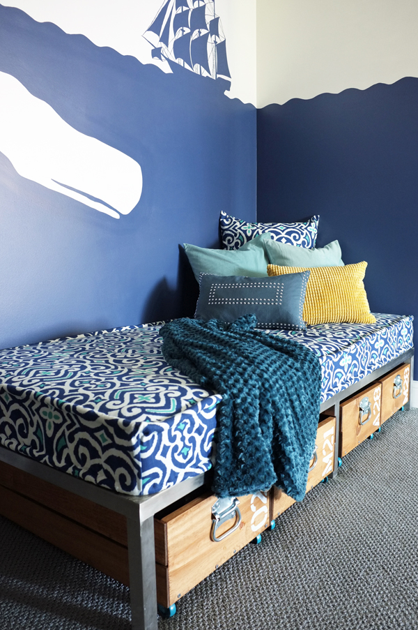 A blue and white bedroom with a bed and drawers styled with a cozy blanket.