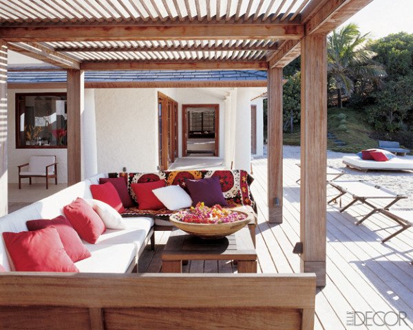 Outdoor wooden deck with white furniture and red pillows.