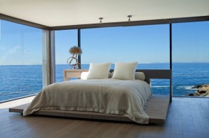 A bedroom with floor to ceiling windows overlooking the ocean.