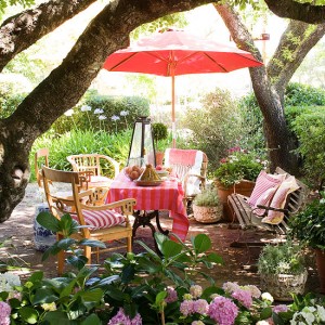 An outdoor living space with a table and chairs under a red umbrella in a garden.