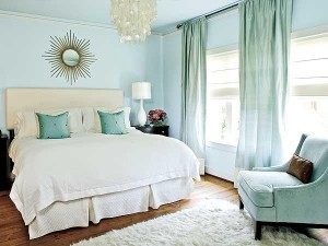 A bedroom with light blue walls and white furniture, decorated with pastels.