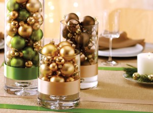 Three festive glass vases with ornaments as holiday table decorations.