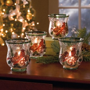 Four festive glass candle holders adorned with birds, placed on a table in front of a beautifully decorated Christmas tree.