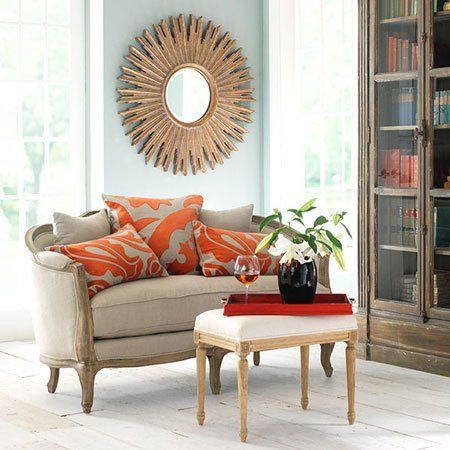 A living room with a sunburst mirror and orange pillows showcases the versatility and style of the settee.