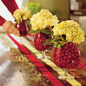 Three festive vases of cranberries on a table.