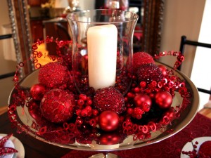 A festive holiday centerpiece with red ornaments and a candle on a silver plate.
