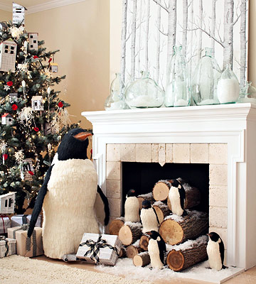 A penguin sits in front of a fireplace adorning a christmas tree.