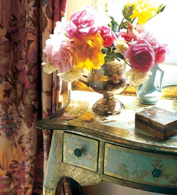 A vase of flowers on a table in front of a window, enhancing a romantic bedroom.