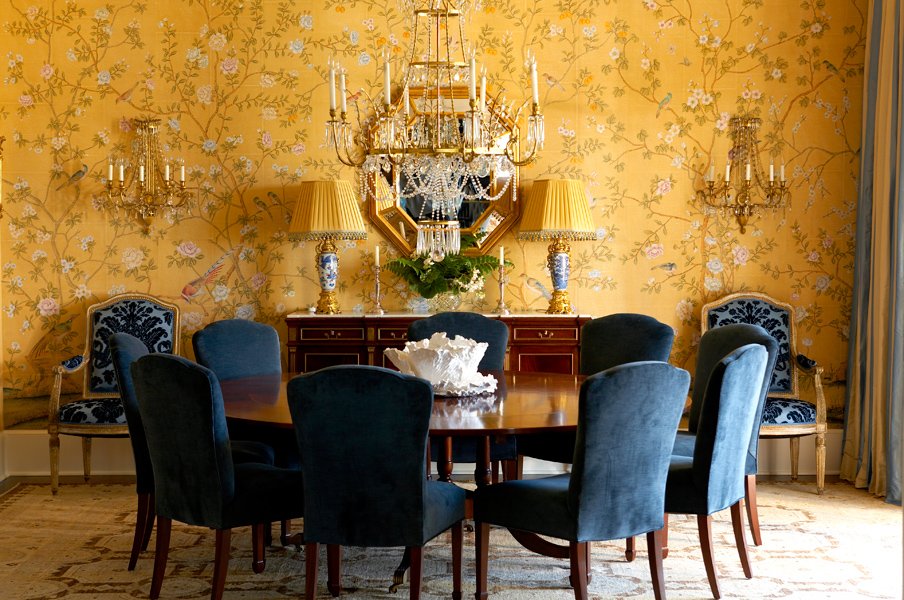 A chic dining room adorned with elegant Chinoiserie-style wallpaper and complemented by blue chairs.