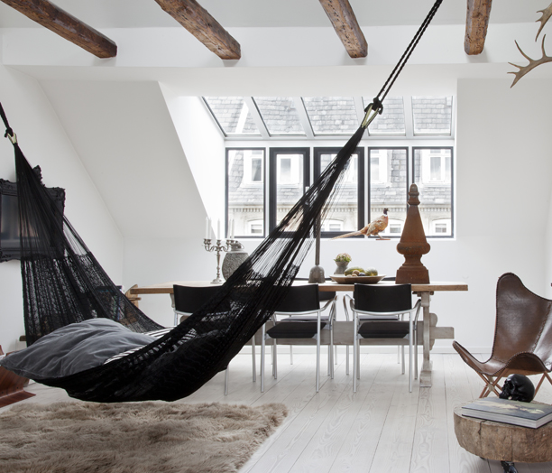 A black hammock swinging from a wooden beam in an indoor setting.