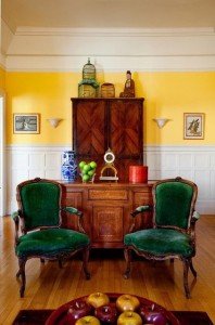 A living room with yellow velvet walls and green velvet chairs.