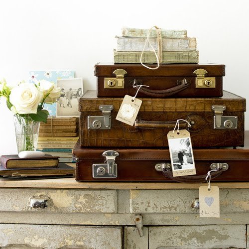 Vintage suitcases with tags on top of a dresser, used for decorating.