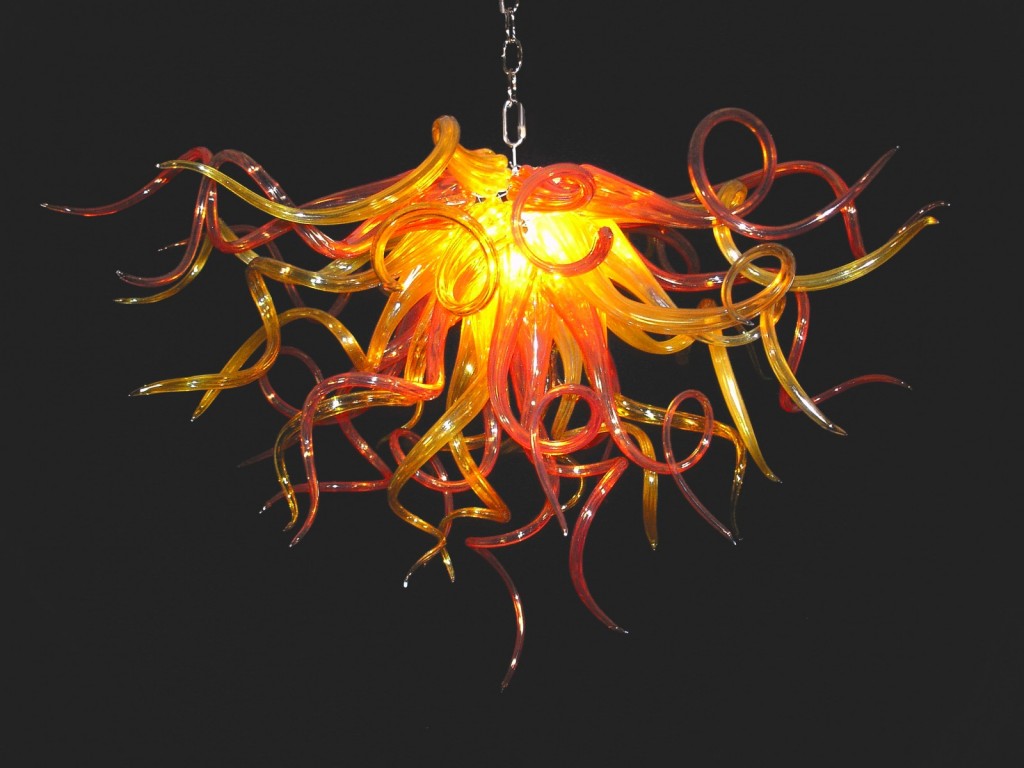 An orange and yellow glass chandelier hanging on a black background that shimmers.