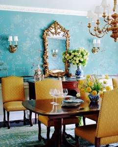 A dining room with bold blue wallpaper and vibrant yellow chairs.