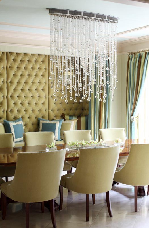 A dining room with beige chairs and a shimmering chandelier.