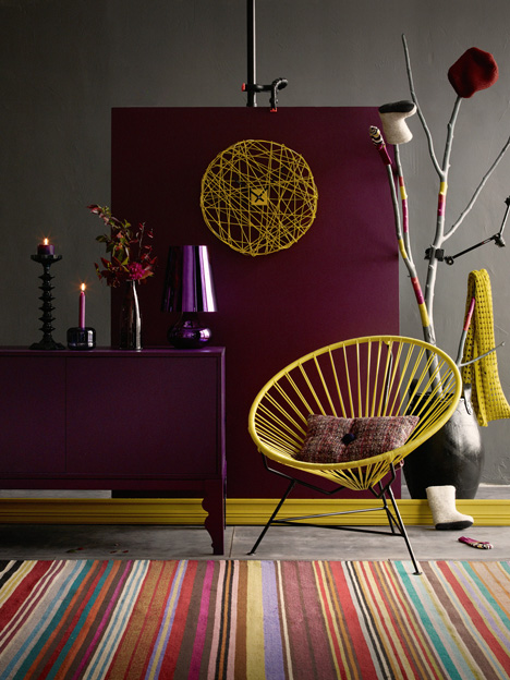 A room with purple walls and a colorful striped rug showcasing interior design trends for 2015.