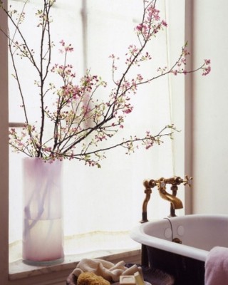 A bathroom with a pink vase and flower arrangements in front of a window.