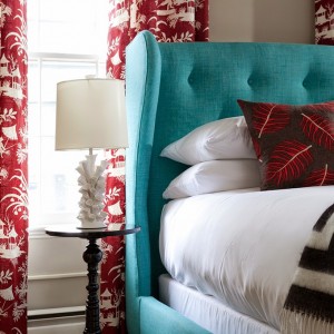 A bed with a turquoise upholstered headboard and marsala pillows.