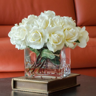 A flower arrangement of white roses in a glass vase on a table.
