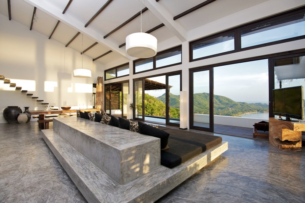 A living room with large windows and concrete flooring overlooking the mountains.