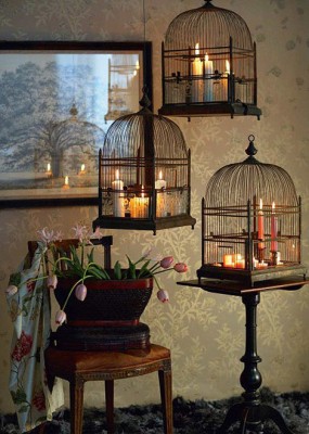 Three vintage bird cages elegantly decorated with hanging candles.