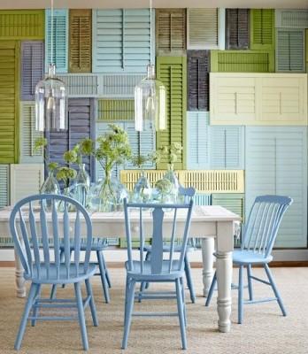 A dining room with blue chairs and colorful shutters.
