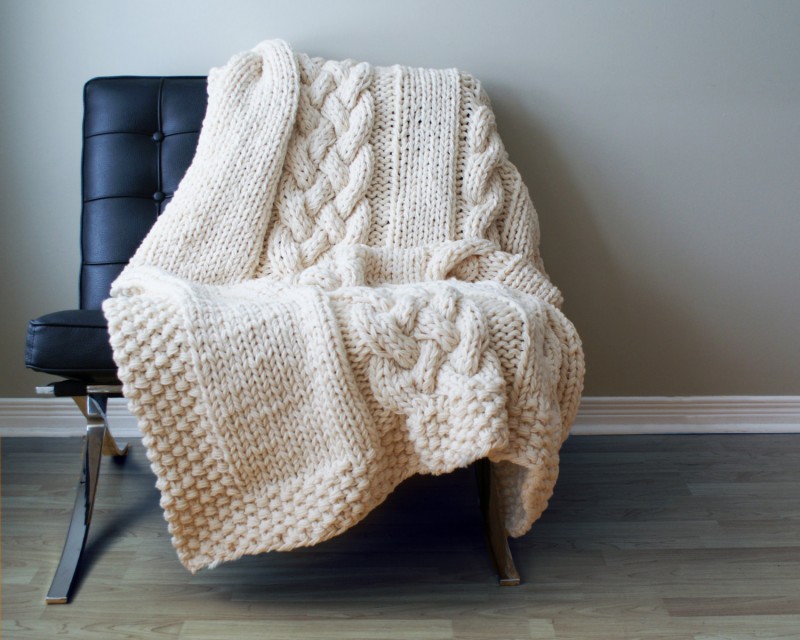 A cable knit throw using knits in your home décor on a chair in front of a wall.