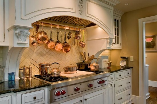 A traditional kitchen with copper pots and pans hanging above the stove.