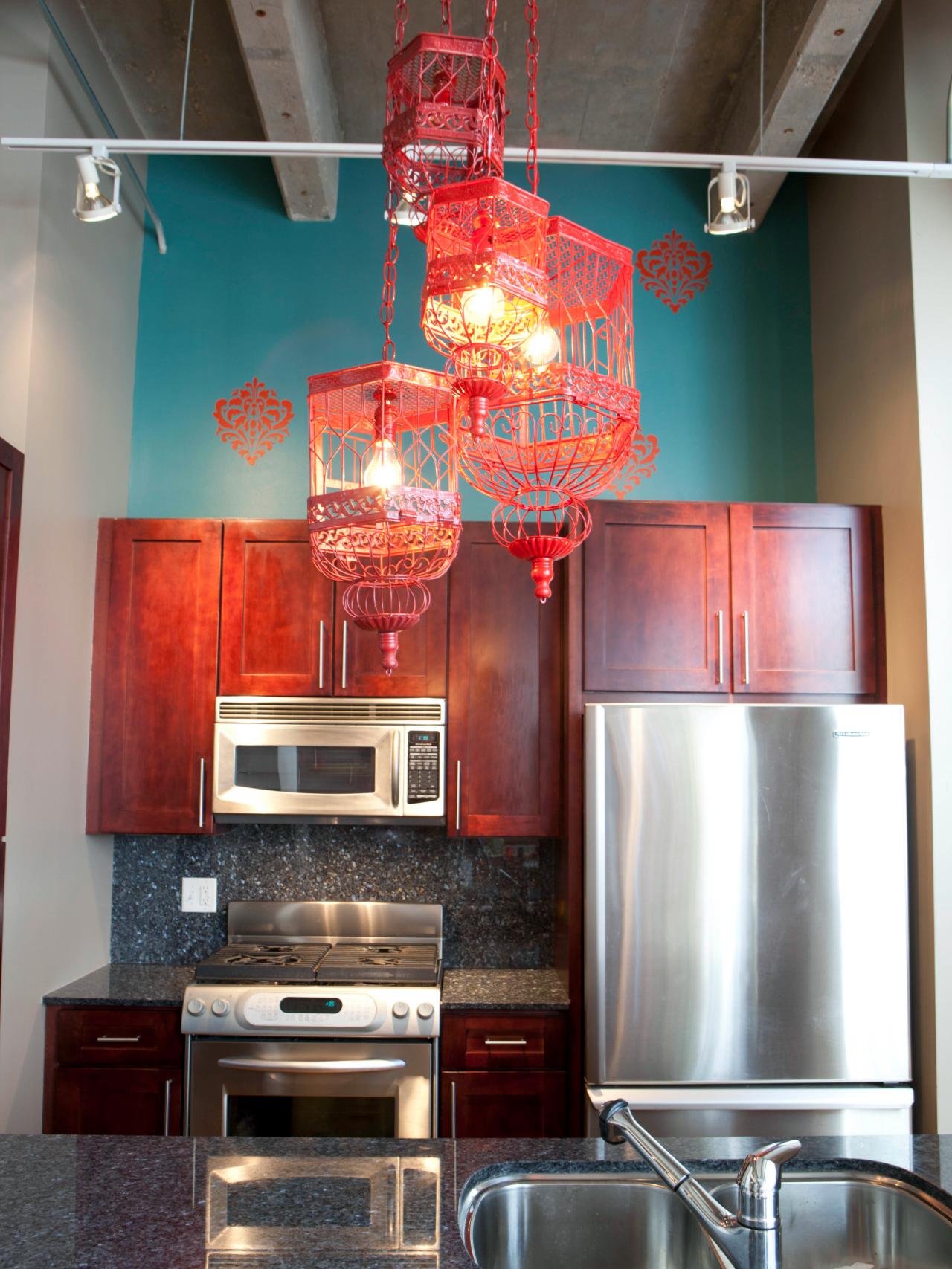 A kitchen with stainless steel sink and red bird cages hanging from the ceiling, with kitchen cabinets.