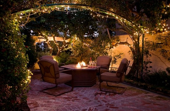 A backyard dining patio with a fire pit and string lights.