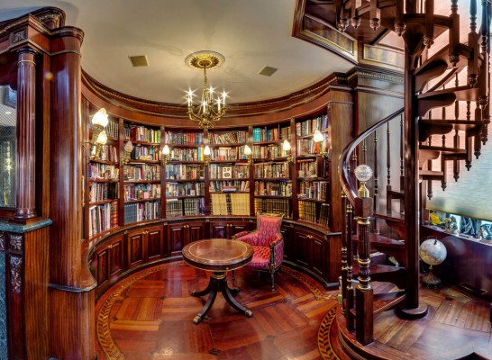 A home library with bookshelves and a spiral staircase.