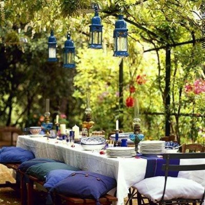 An outdoor dining table with blue lanterns hanging over it in a backyard setting.