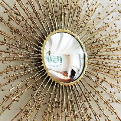 A gold spring-themed sunburst mirror on a wall.