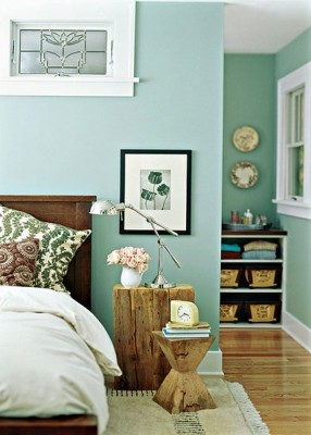 A bedroom with green walls and a wooden bed featuring a styled bedside table.