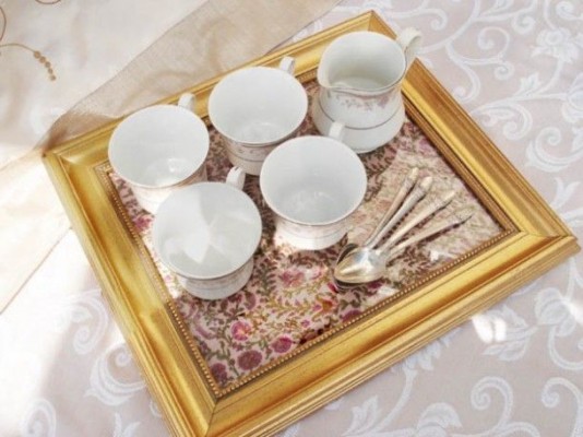 A tray with cups and spoons on it, with picture frames.