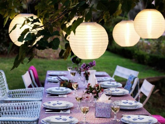 White paper lanterns hanging over a backyard dining table.