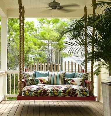 A swing bed on a front porch with a fan.
