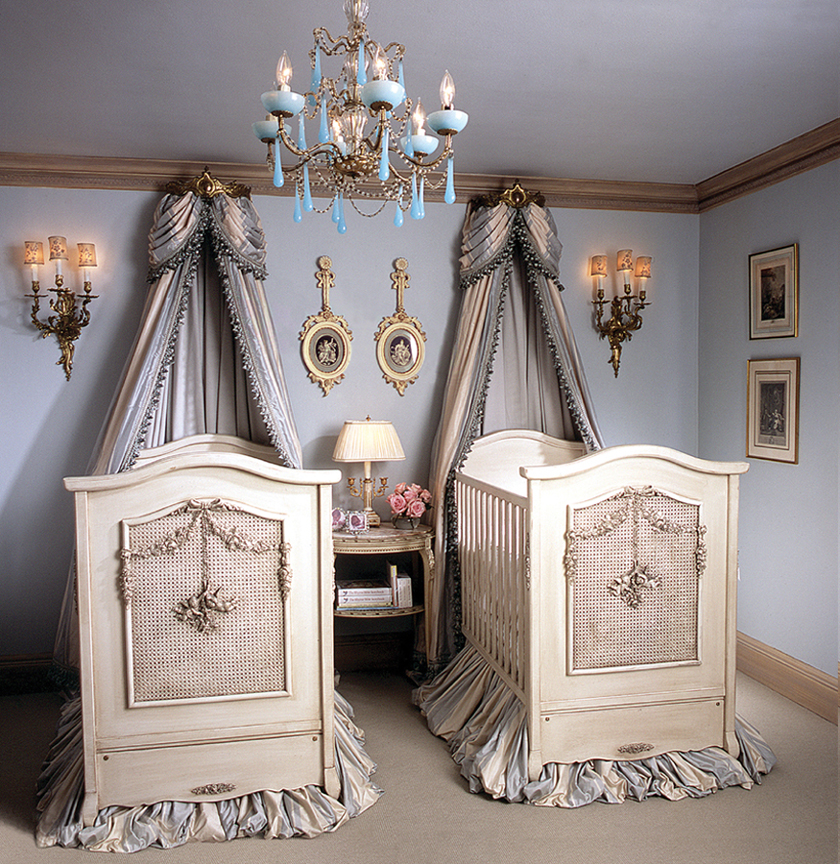 A nursery with two cribs and a chandelier.