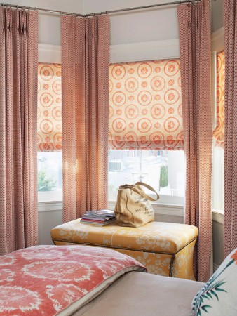 A bed with a pink and orange comforter and window treatments.